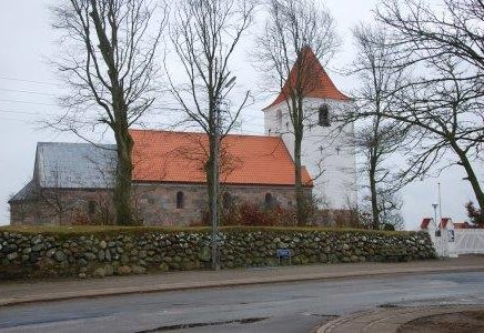 Ørding Kirke med kirkedige og en vej i forgrunden. Der er ingen blade på træerne.