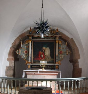 Stor stjerne hænger fra loftet. I baggrunden ses alter og altertavle med en lysestage.